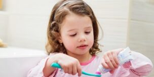 Little girl in bathroom putting a toothpaste on toothbrush